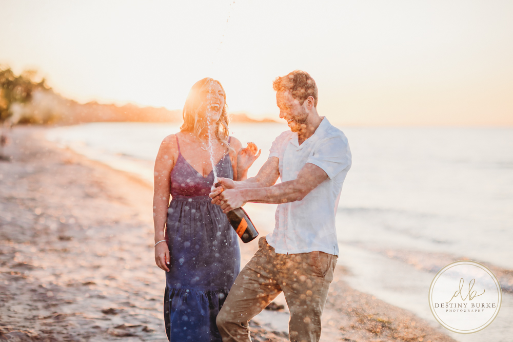 Engagement Session with Couple at Durand Eastman Beach in Irondequoit, NY near Rochester at sunset with champagne toast, engagement ring