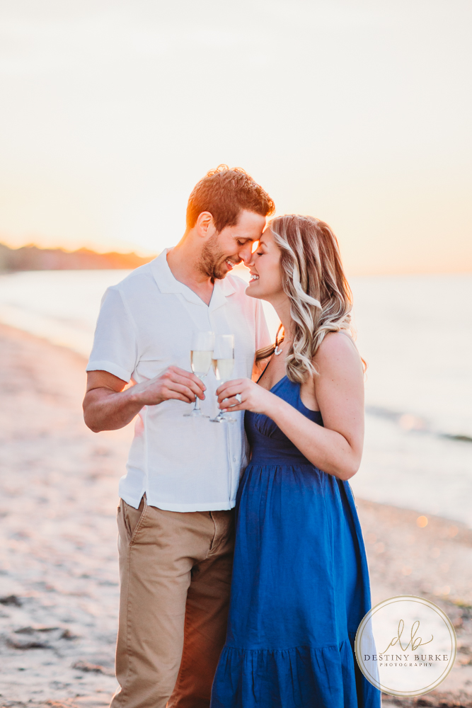 Engagement Session with Couple at Durand Eastman Beach in Irondequoit, NY near Rochester at sunset with champagne toast, engagement ring