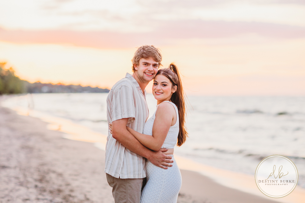Durand Eastman Park in Irondequoit, NY, Couple poses for Engagement portrait photography session at sunset on the beach , portraits done by Destiny Burke Photography