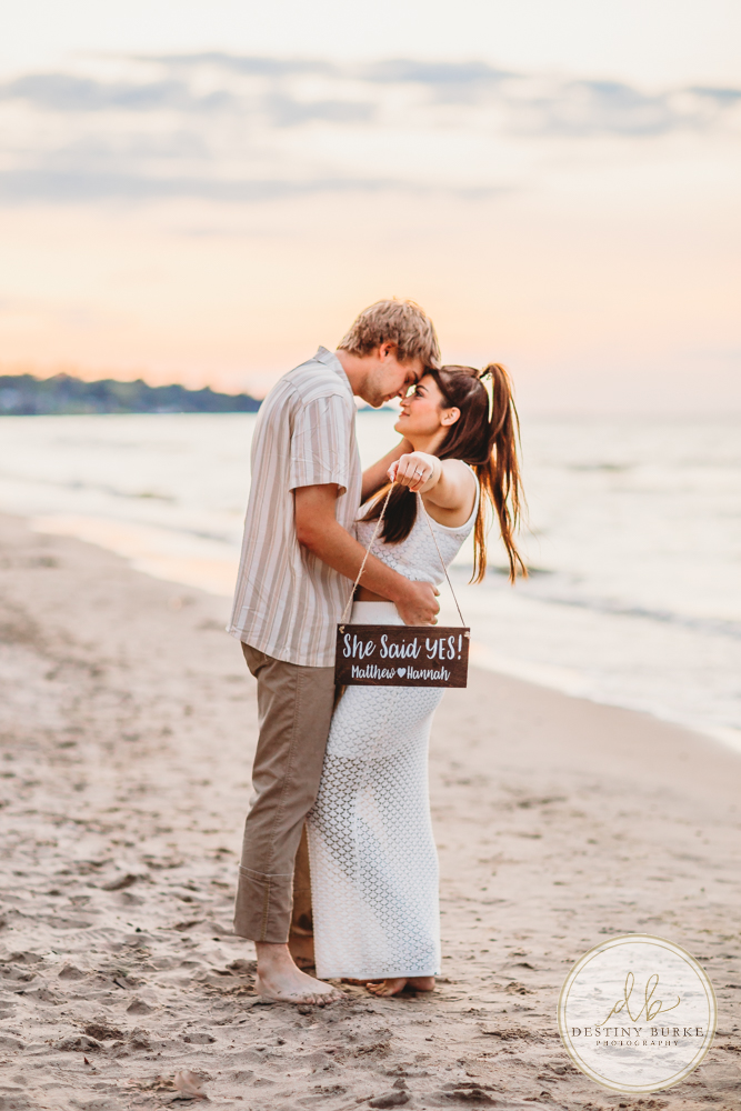 Durand Eastman Park in Irondequoit, NY, Couple poses for Engagement portrait photography session at sunset on the beach , portraits done by Destiny Burke Photography