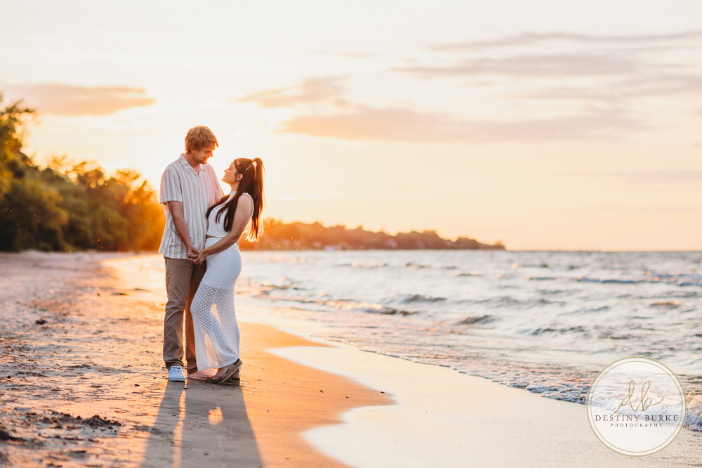 Durand Eastman Park in Irondequoit, NY, Couple poses for Engagement portrait photography session at sunset on the beach , portraits done by Destiny Burke Photography