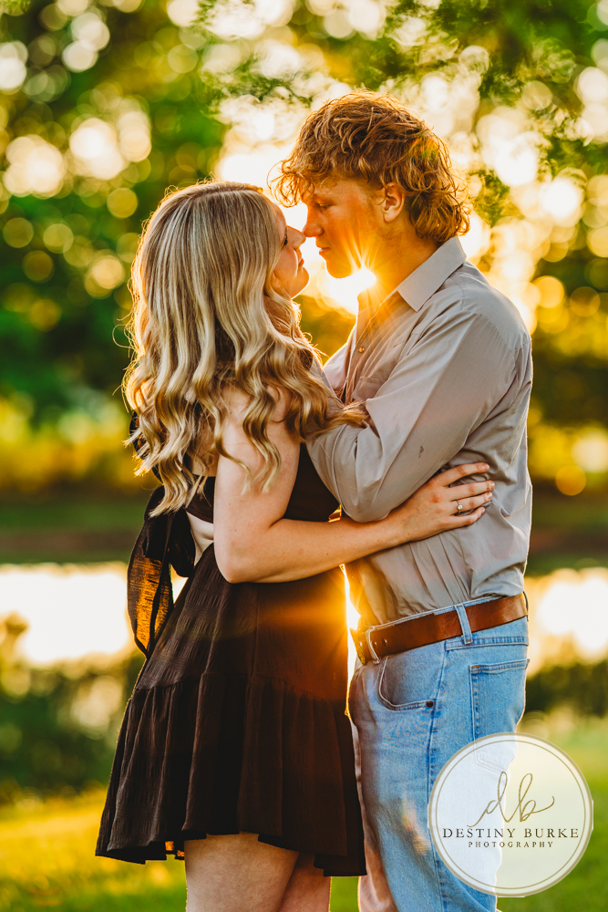 Romantic golden hour engagement portrait of a couple embracing with the sun glowing between them during a sunset couples session by a Rochester NY engagement photographer.