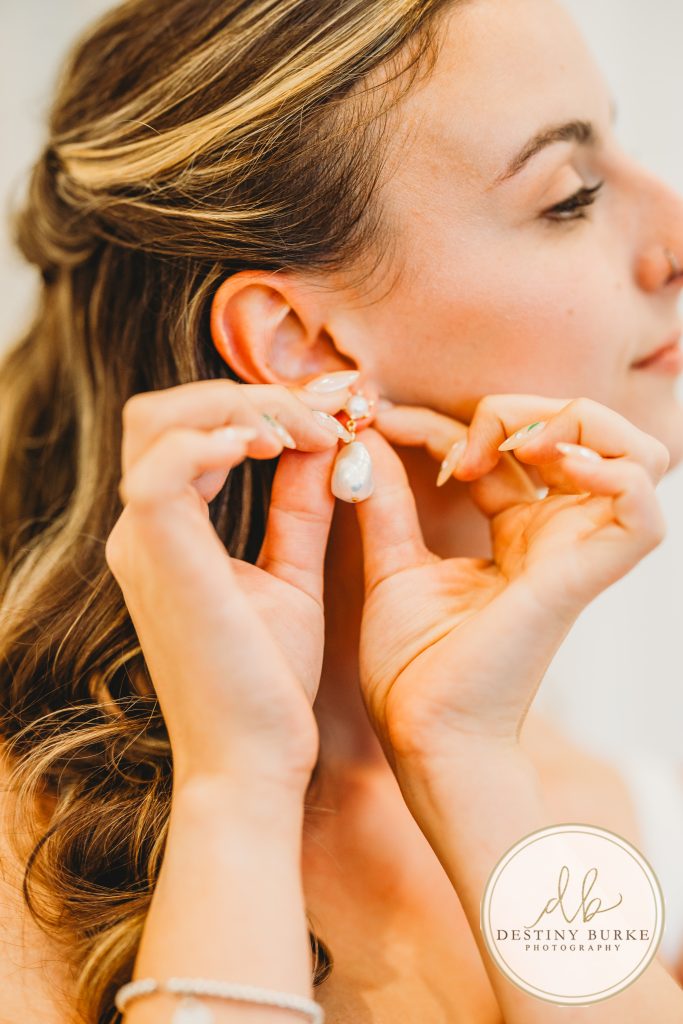 Bride putting on pearl wedding earrings before ceremony at Pomona at Blue Barn in Hilton NY